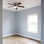 Bedroom with light blue walls, white trim, vinyl plank flooring, and a ceiling fan.