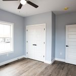 Bedroom with light blue walls, white closet doors, white trim, vinyl plank flooring, and a ceiling fan.