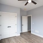 Bedroom with light blue walls, white trim, vinyl plank flooring, white closet doors, and a ceiling fan.