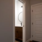 Hallway leading into a bathroom with a brown sink vanity and light colored walls.