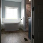 Bathroom with light blue walls, vinyl plank flooring, white trim, a white tub beside a ship lap wall, and a standing shower with marble chevron tiles.