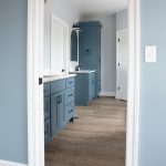 A bathroom with light blue walls, white trim, vinyl plank flooring, and dark blue sink vanity cabinets with white countertops.