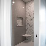 Standing shower with gray tiles and a marble chevron accent wall.