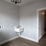 Laundry room with light colored walls, vinyl plank flooring, a white sink, and an open doorway leading into a hallway.