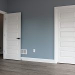 Bedroom with blue walls, white trim, 2 white doors, and vinyl plank flooring.