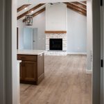 Combined kitchen and living area with a wood kitchen island, light stone countertops, vinyl plank flooring, light colored walls, a white washed brick fireplace, and decorative wood ceiling beams.