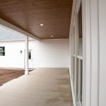 Covered front porch with a wood plank ceiling, white puck ceiling lights, and a cement porch floor attached to a home with white sliding.