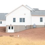 Left side exterior of a home with white siding, gray asphalt roofing, and a set of white basement doors.