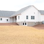 Back and left side exterior of a home with white siding, gray asphalt roofing, a set of white basement doors, and a covered back patio.