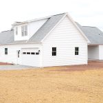 Back and right side exterior of a home with white siding, gray asphalt roofing, a white single-entry side door, and a white garage door with windows.