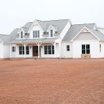 Front and right side exterior of a home with white siding, gray asphalt roofing, brick veneer, decorative shakes, a covered front porch, a white garage door with windows, and a white single-entry side door.