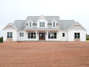 Front exterior of a home with white siding, gray asphalt roofing, brick veneer, decorative shakes, a covered front porch, and brown double doors.