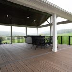 New covered deck with brown flooring, white beams and posts, black aluminum railings, a black outdoor dining set, a hot tub, and a brown plank ceiling with puck lights.