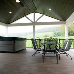 New covered deck with brown flooring, white beams and posts, black aluminum railings, a black outdoor dining set, a hot tub, and a brown plank ceiling with puck lights.