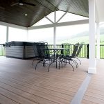 New covered deck with brown flooring, white beams and posts, black aluminum railings, a black outdoor dining set, a hot tub, and a brown plank ceiling with puck lights.