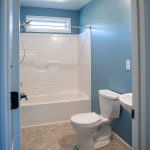 Bathroom with blue walls, a white shower and tub, a white toilet, and tan tile flooring.