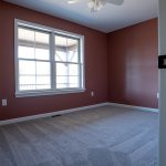 Room with red walls, gray carpeting, a white set of windows, and a white ceiling fan.