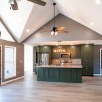 Kitchen with green cabinets, a green kitchen island with white countertops, stainless steel appliances, brown walls, a white vaulted ceiling, a black and brown ceiling fan, and vinyl plank flooring.