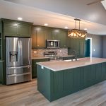 Kitchen with green cabinets, white countertops, gray and white tile backsplash, a matching kitchen island with a black sink faucet, stainless steel appliances, brown walls, and a white ceiling.