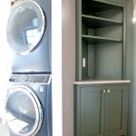 Stacked washer and dryer with a tall, green cabinet and shelves on the other side of the wall.