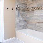 Gray and white tiled shower and tub combo with decorative accent tiling, a light gray and white floor, and brown walls.