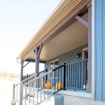 Front porch on a new, ranch-style home with concrete steps, black railings, blue siding, white windows, and brown posts.