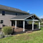 New covered deck with brown decking, white beams, white posts, and black aluminum railings.